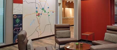 A hotel lobby with a map on the wall, leather seating, a small table, and a reception area in the background.