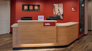 A reception desk with a 'hello.' sign, two monitors, and a framed 'Stay, Work, Play' sign on the wall.