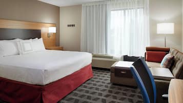 A hotel room with a large bed, a desk with a chair, a sofa, and a window with curtains.