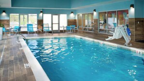 An indoor swimming pool with clear blue water, surrounded by blue chairs and tables, and large windows offering a view of the outside. - TownePlace Suites by Marriott Richmond (Richmond)