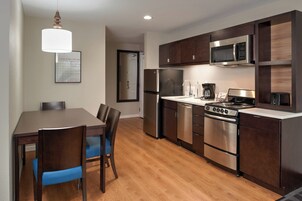 Una cocina moderna con armarios de madera oscura, electrodomésticos de acero inoxidable y una mesa de comedor de madera con sillas azules.