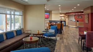 A hotel lobby with a sofa, chairs, a coffee table, a reception desk, and a TV screen displaying 'TOWNSHIP PLACE'. - TownePlace Suites by Marriott Richmond (Richmond)