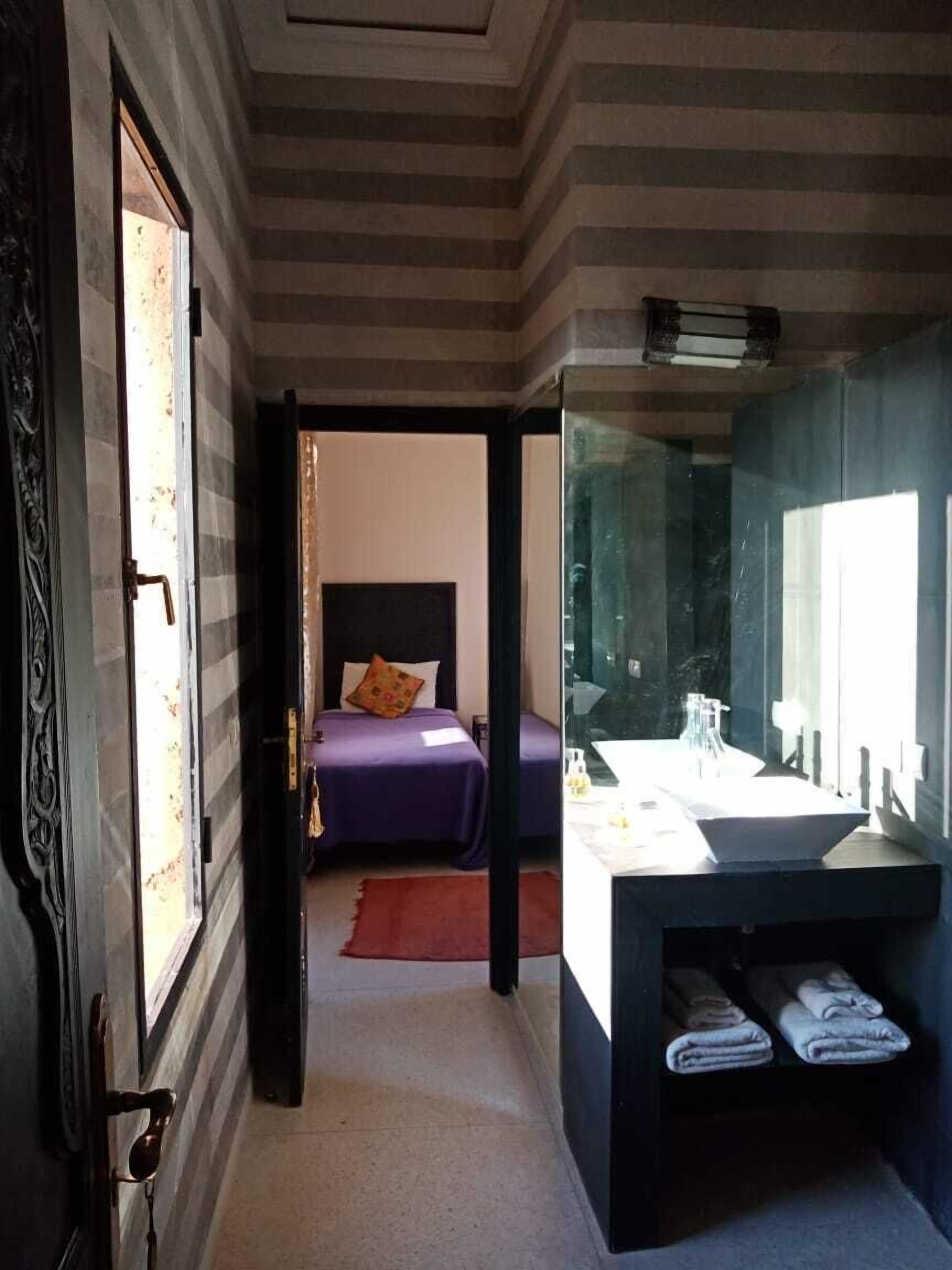 A hotel room with a bed, a bathroom with a mirror, and a door leading to another room.