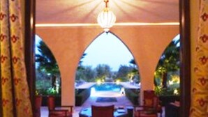 Un patio al aire libre con mesa y sillas, un colgante de luz y vistas a una piscina y follaje.