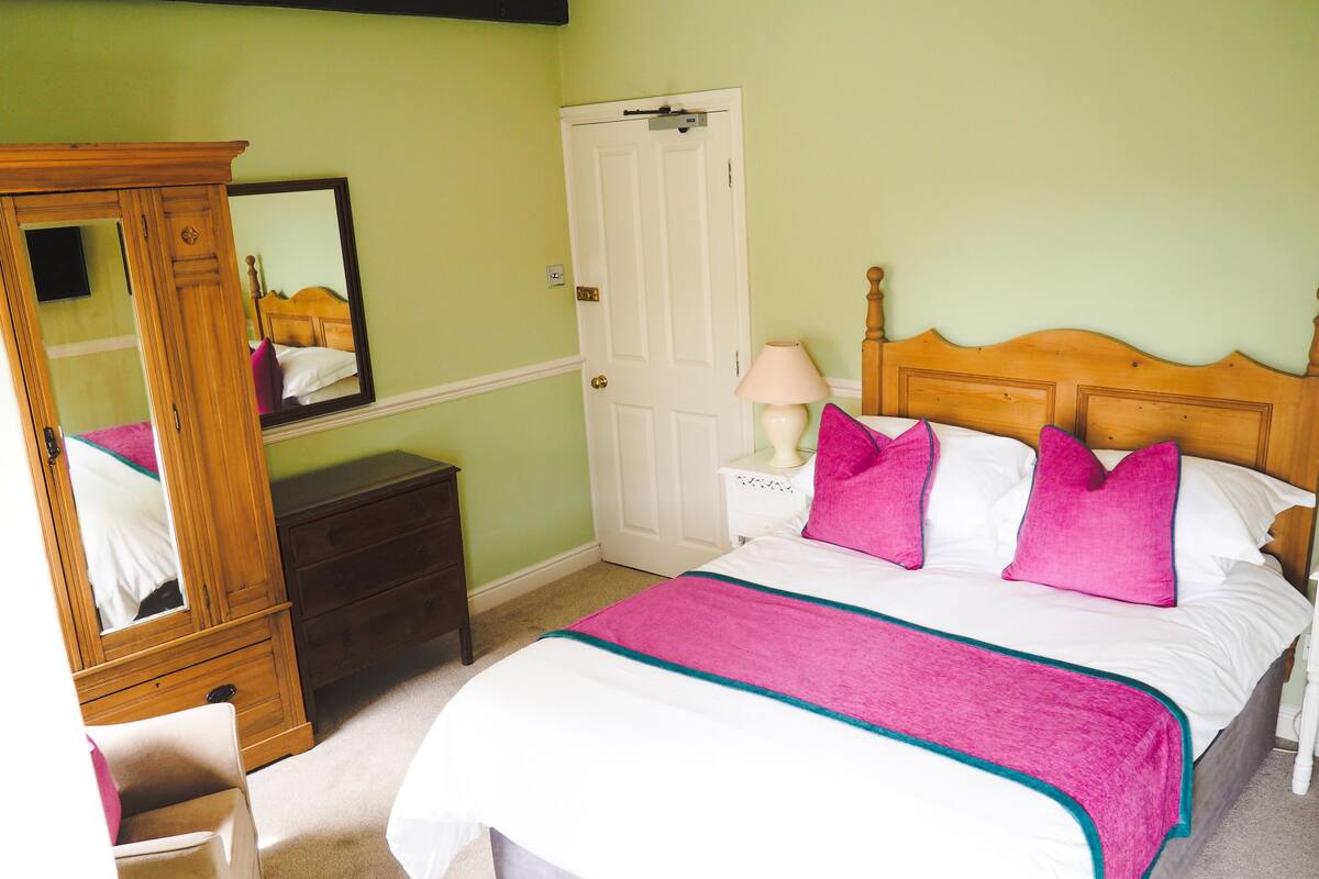 A bedroom with a bed, a nightstand, a dresser, a mirror, and a door.