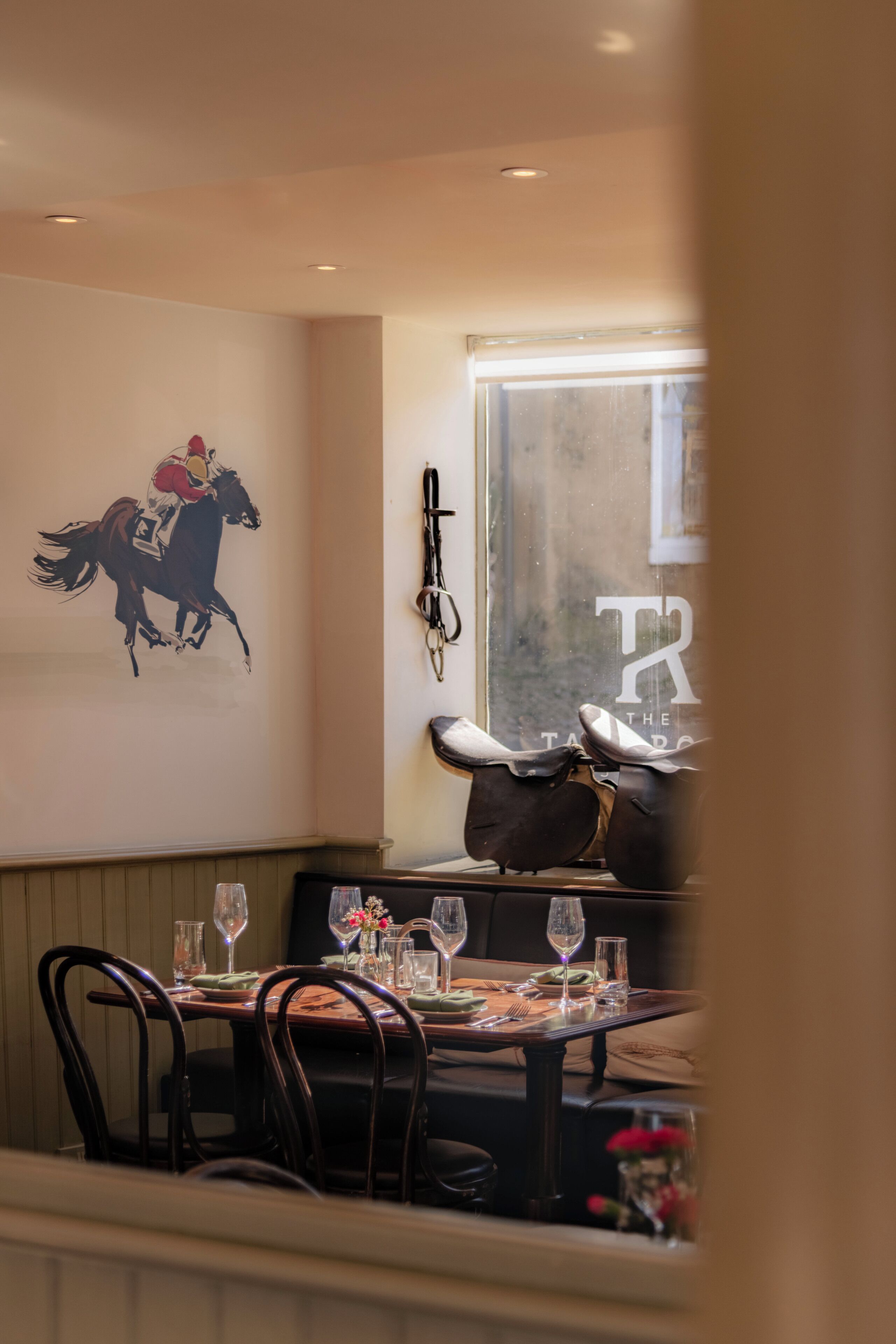 Um restaurante com um mural de cavalos, uma janela com vista e uma mesa posta para refeição.