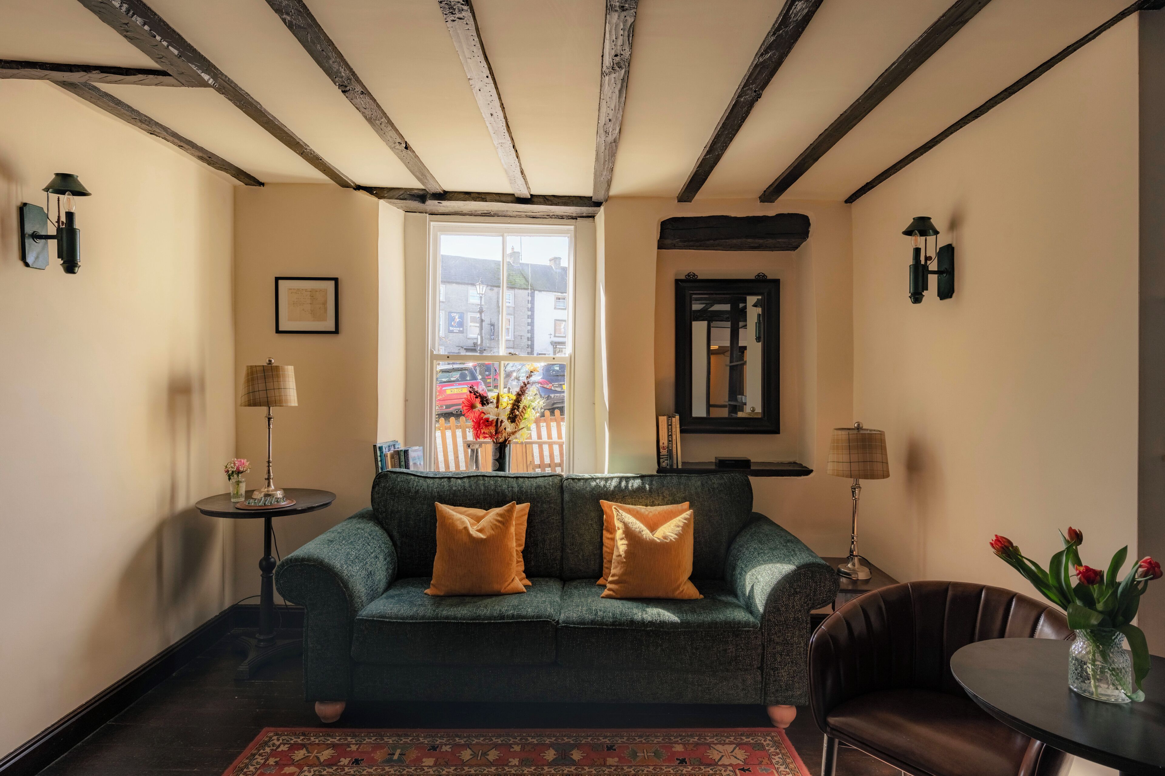 Una habitación con un sofá verde, una mesita con una lámpara, una ventana con vistas y un espejo en la pared.
