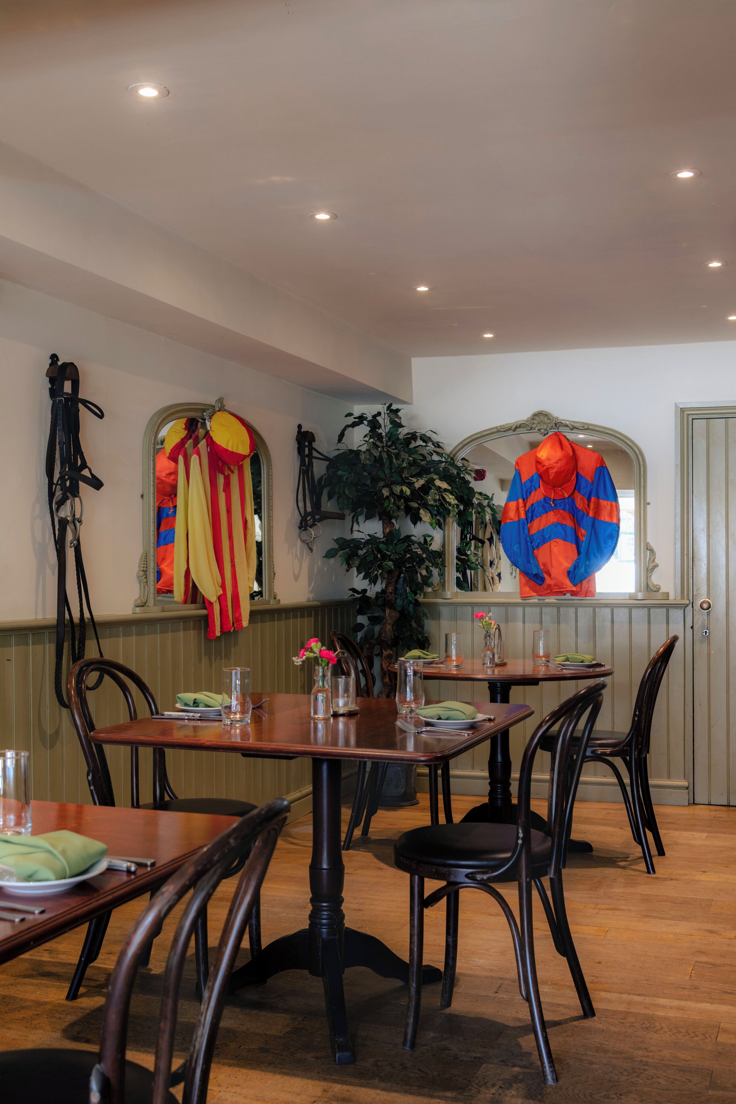 A dining area with wooden tables and chairs, a mirror, and a potted plant.
