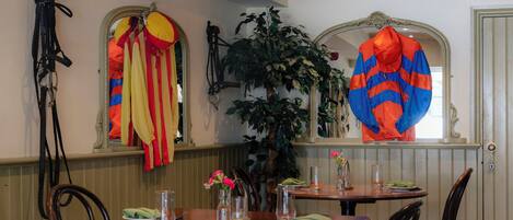 Un comedor con mesas y sillas de madera, un espejo y una planta en maceta.