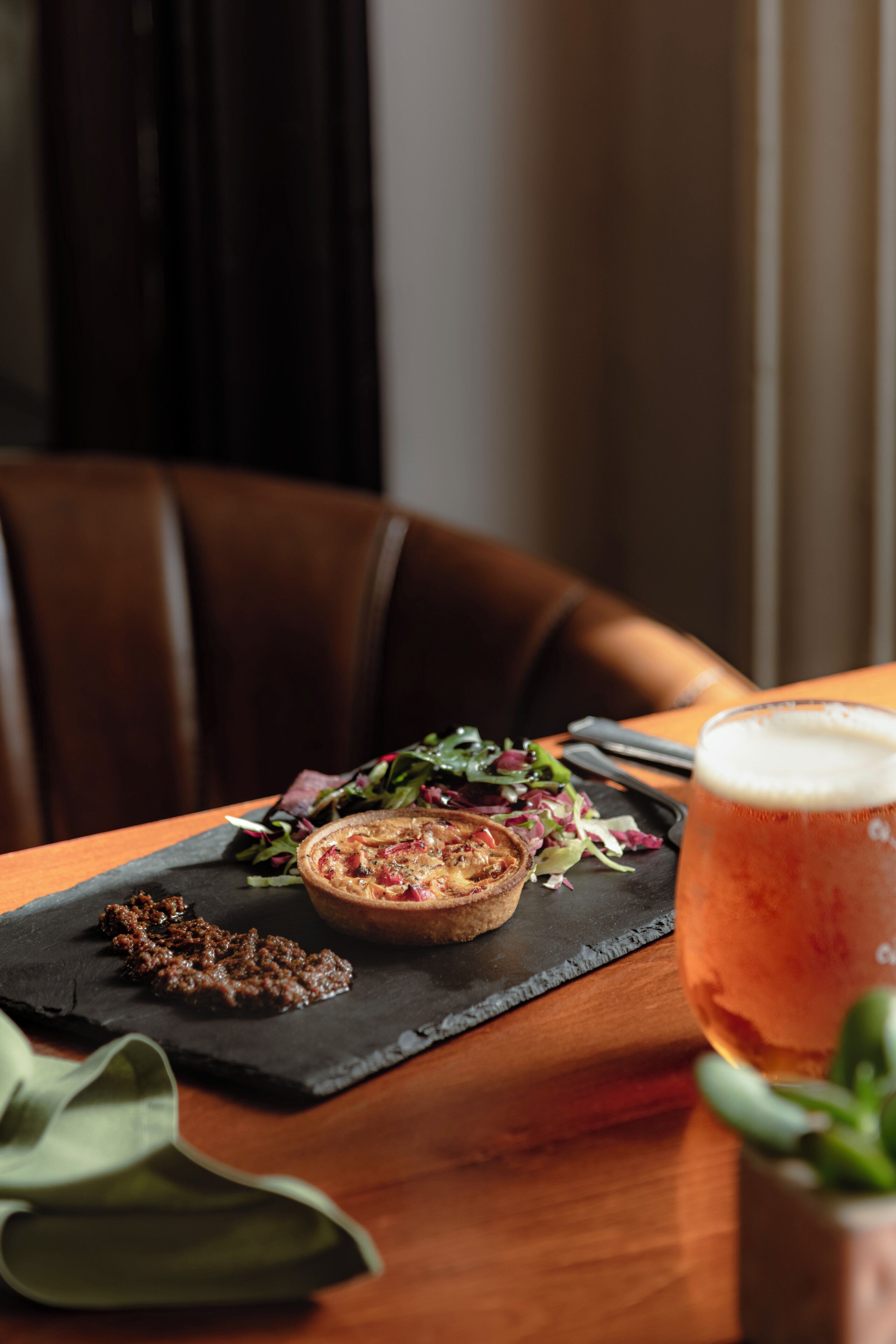 A dining table with a pizza, salad, and a glass of beer.