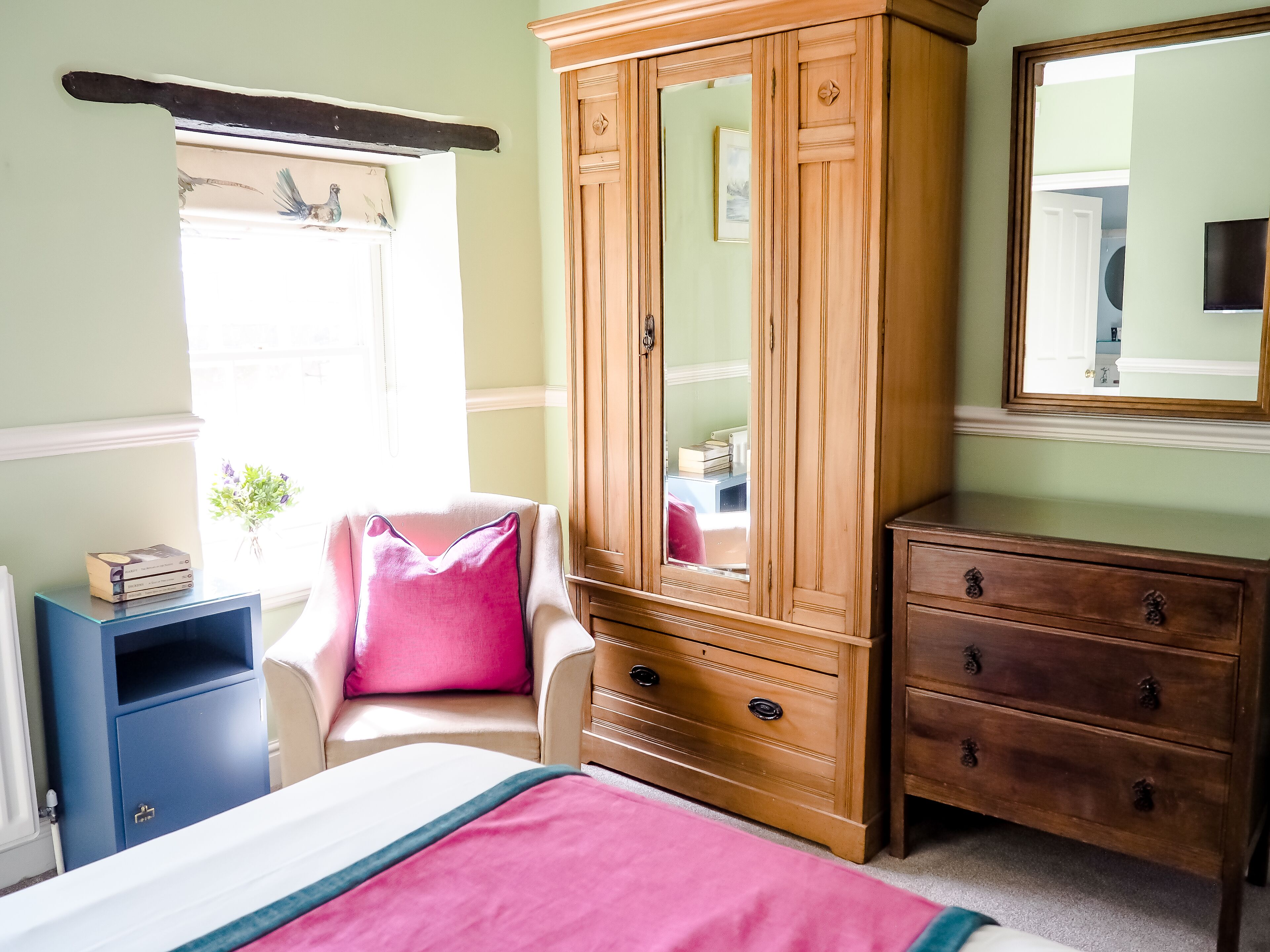 Un dormitorio con una cama, un armario de madera, una silla, un tocador y un espejo.