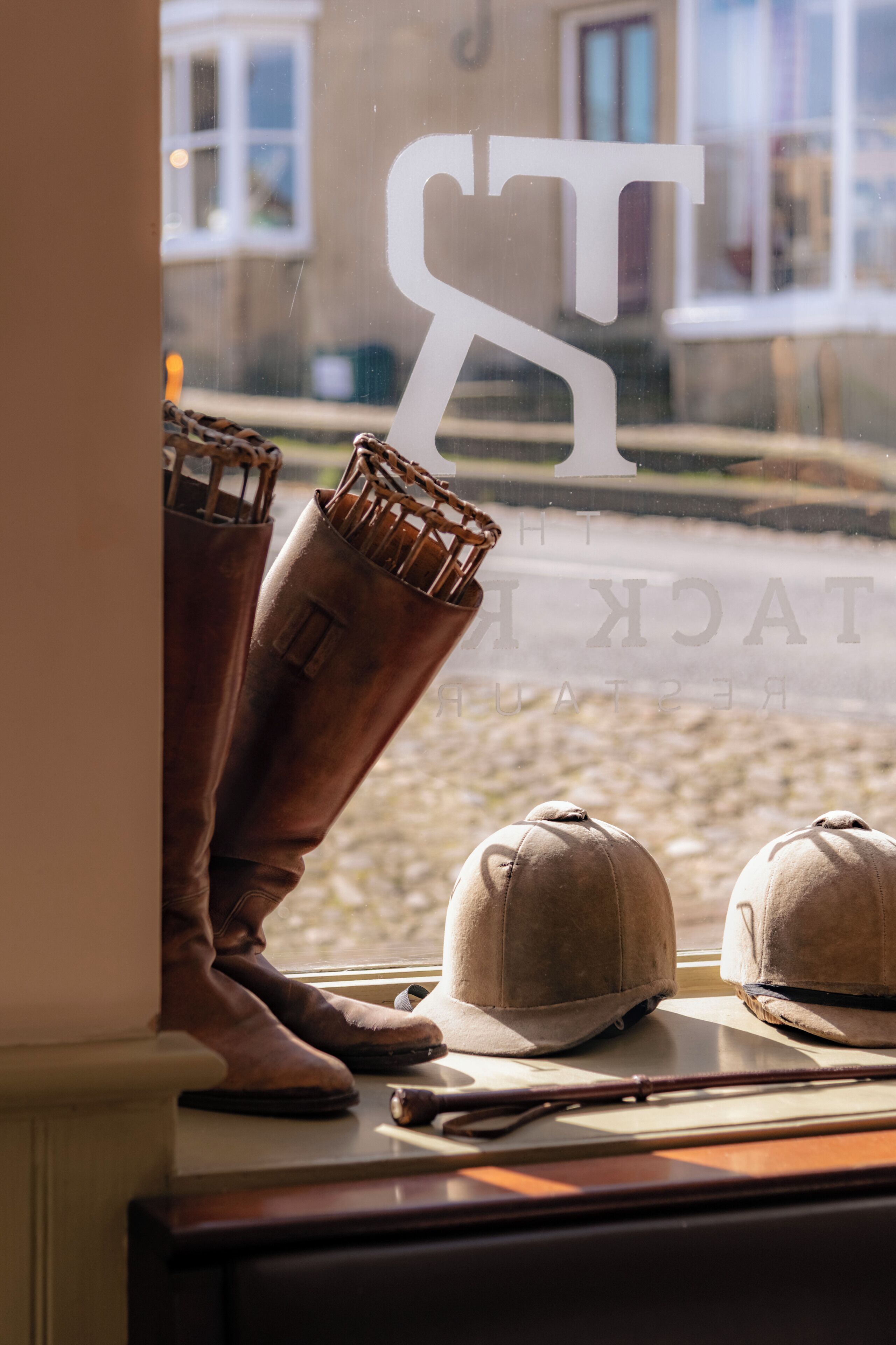 A window with a view of a building, a pair of boots, and two hats on a ledge.