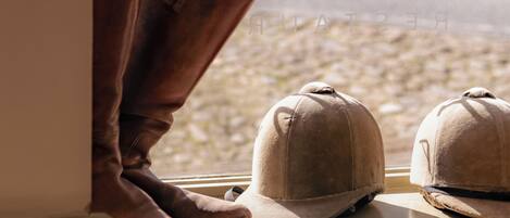A window with a view of a building, a pair of boots, and two hats on a ledge.