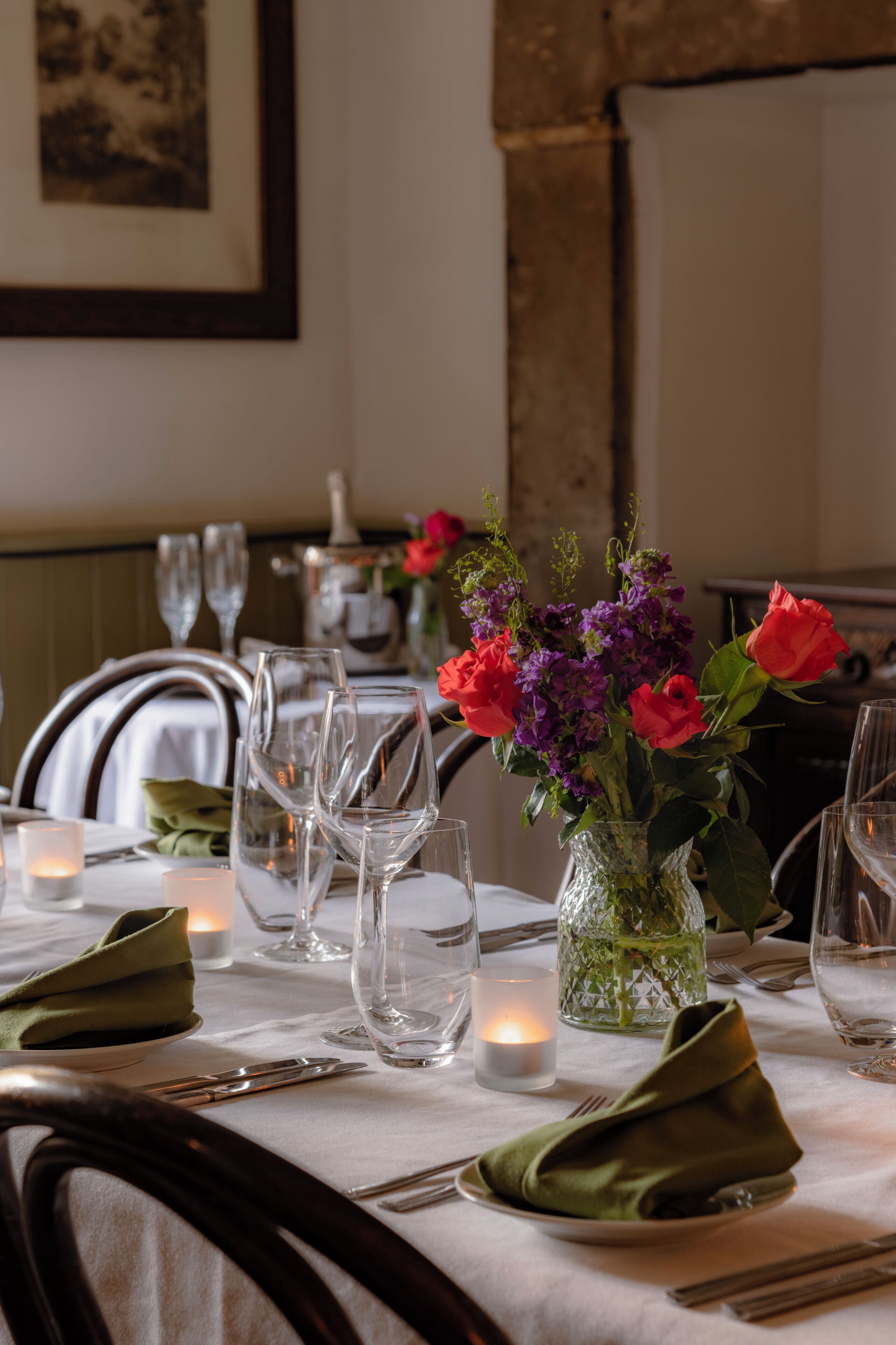 Een eettafel gedekt met borden, bestek, glazen en een vaas met bloemen.