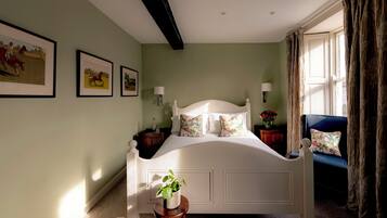 A bedroom with a bed, a chair, a nightstand, a lamp, and wall art.
