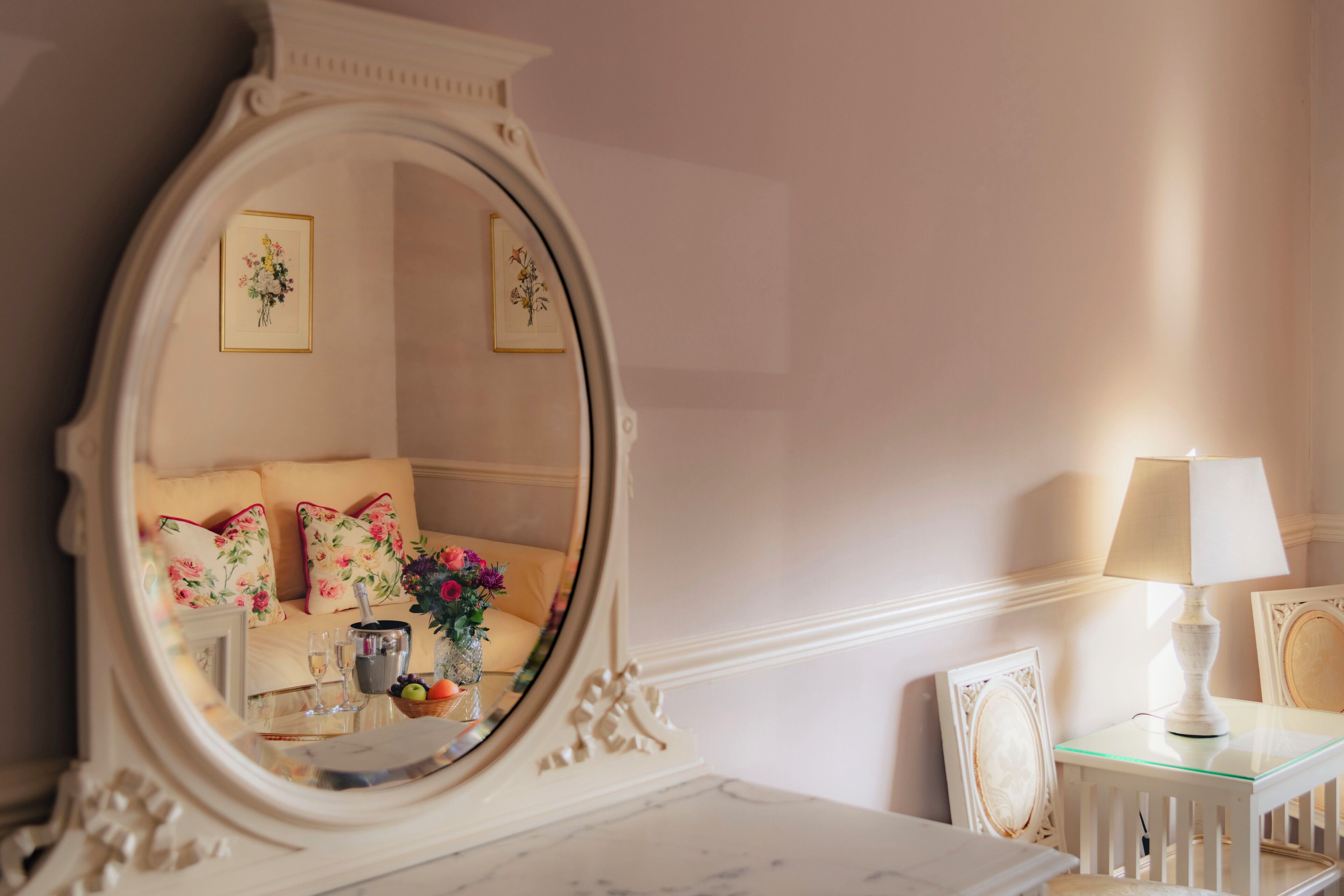 Una habitación con un espejo grande, un sofá con cojines estampados, una mesita con una lámpara y cuadros en la pared.