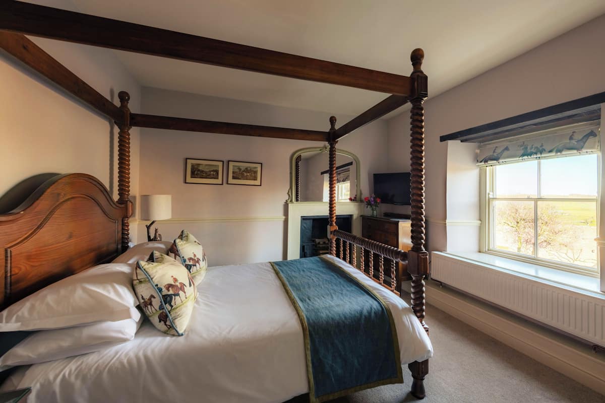 A four-poster bed with a wooden headboard, a blue throw blanket, and decorative pillows.