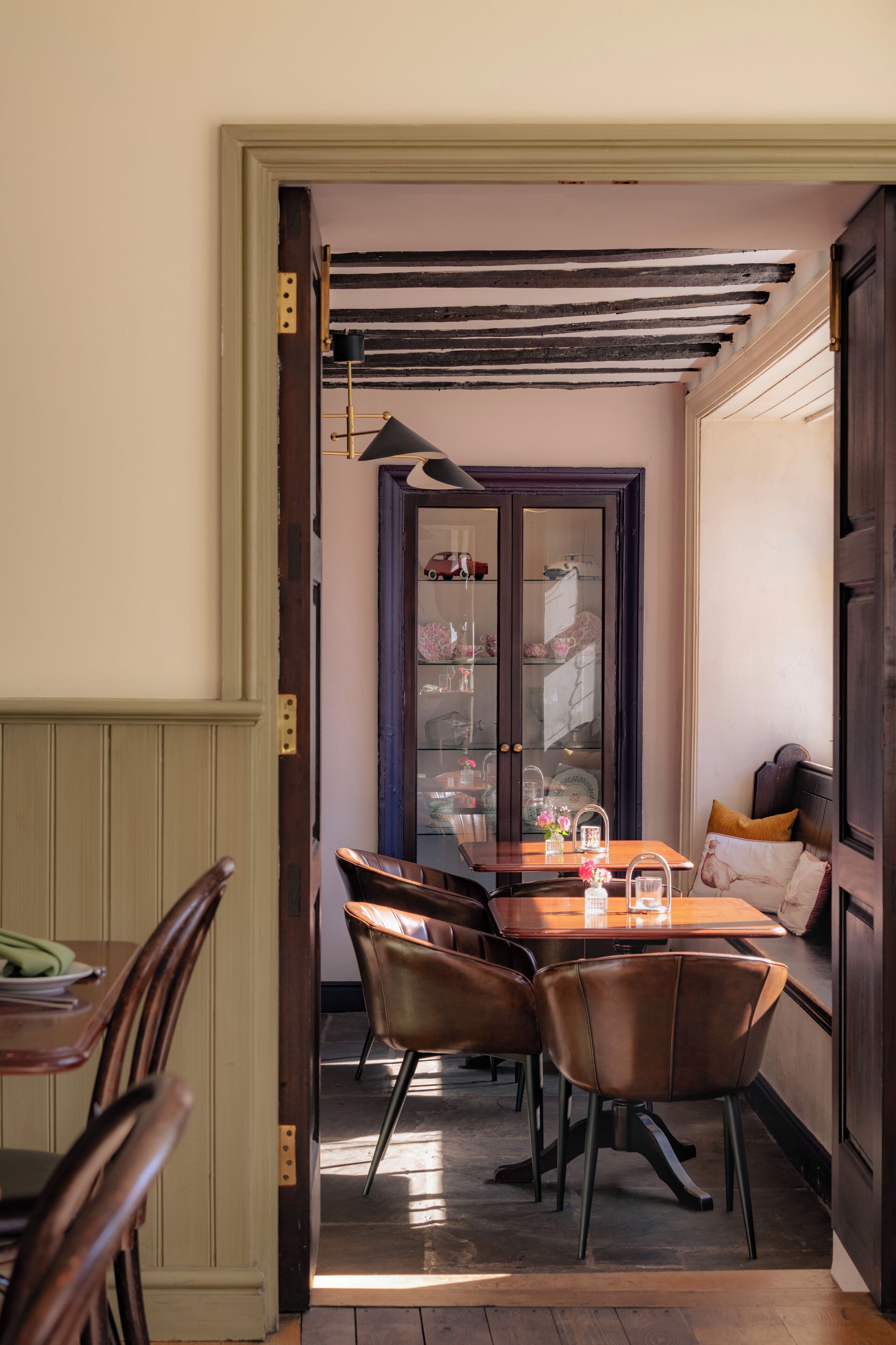 Un comedor con una mesa y sillas de madera, un aparador con puertas de cristal y un banco con cojines.