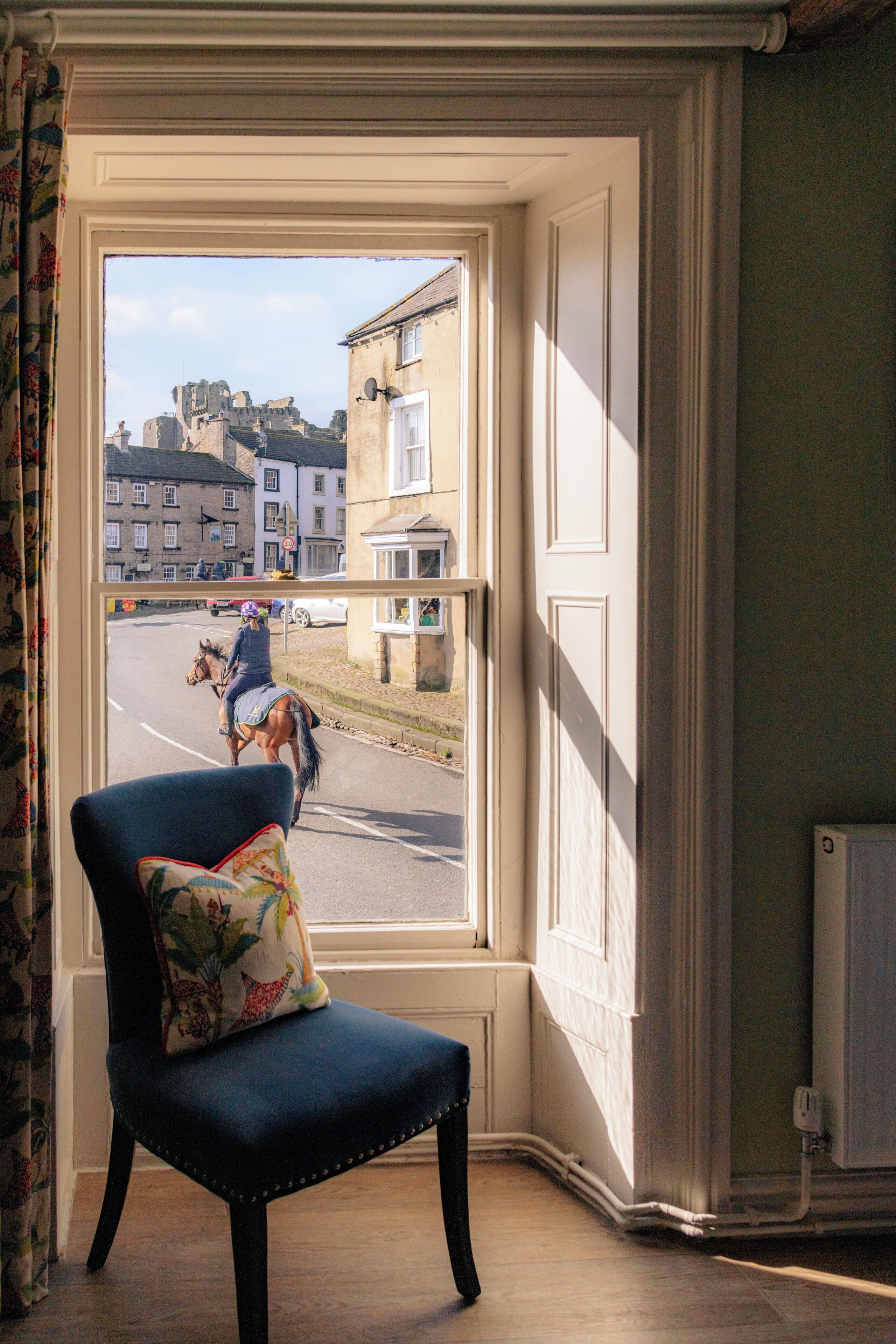 A room with a window overlooking a street, a chair with a floral cushion, and a radiator.
