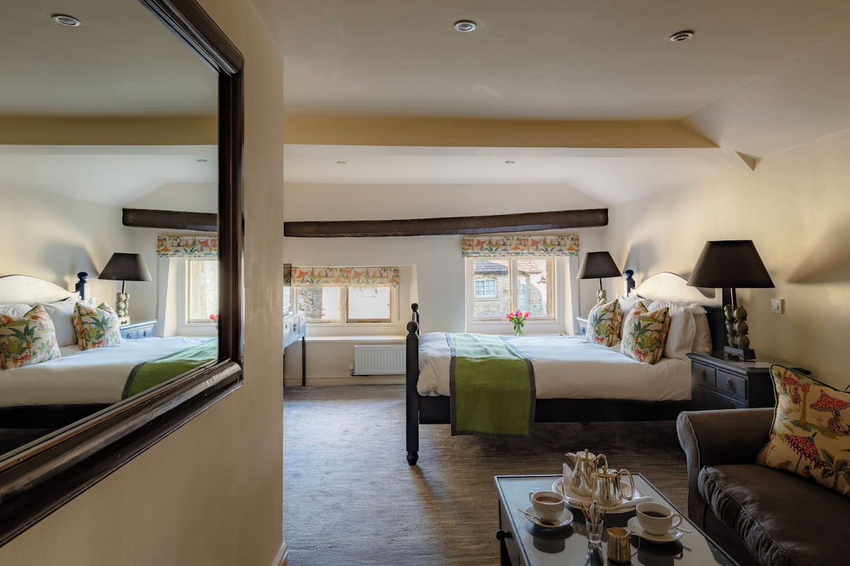A hotel room with two beds, a sitting area, a coffee table with tea set, and a large mirror.