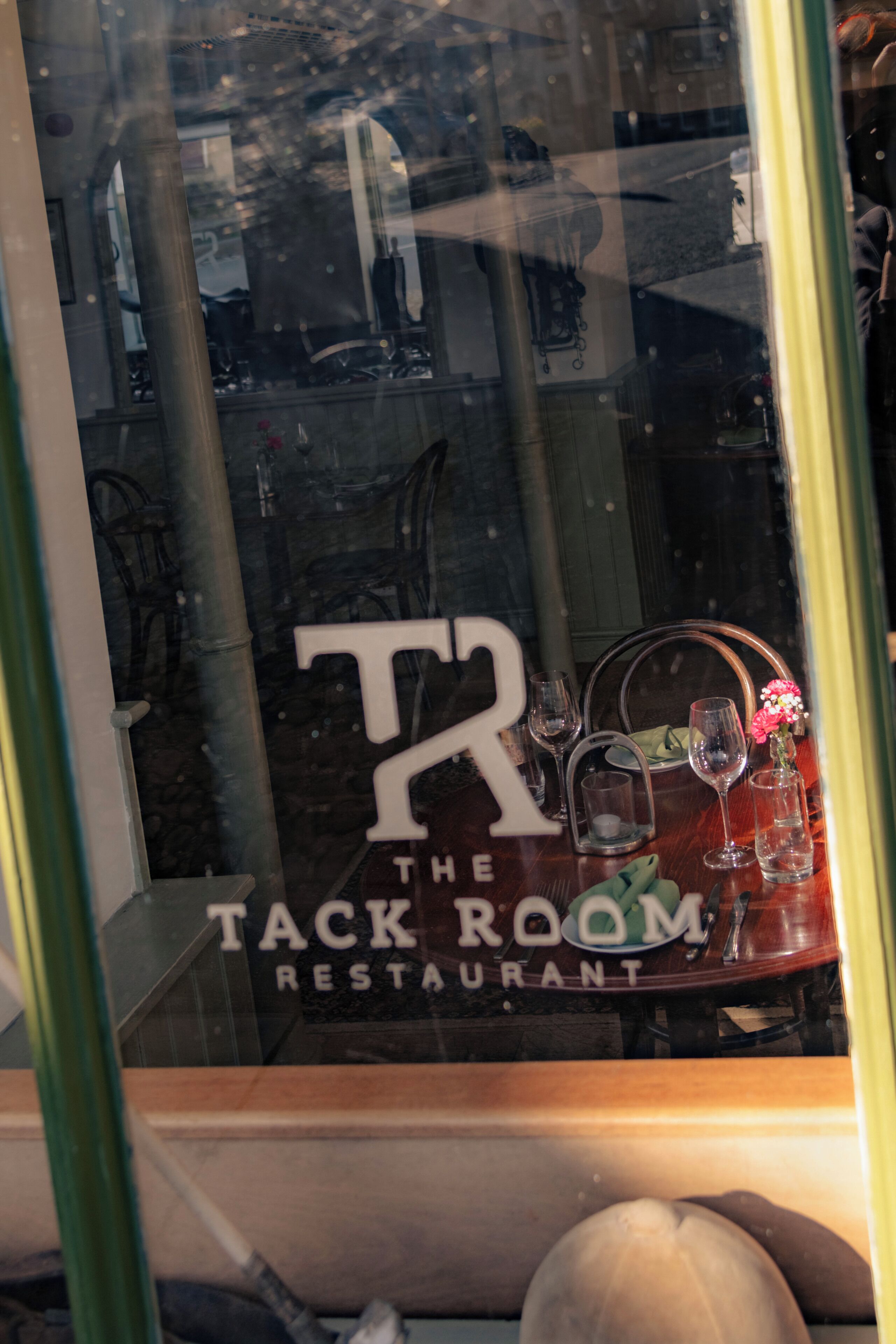 A restaurant window with the sign 'TACK THE ROOM RESTAURANT' and a table with wine glasses and a vase.