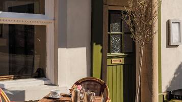 Una mesa con sillas frente a un edificio, una planta en maceta y una puerta con placa.