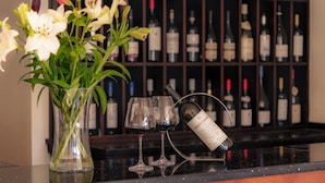 Una zona de bar con una botella de vino, copas y un jarrón con flores.