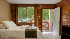 A hotel room with a bed, a window with curtains, a door, and a view of the outside. - Santval (Cumanda)