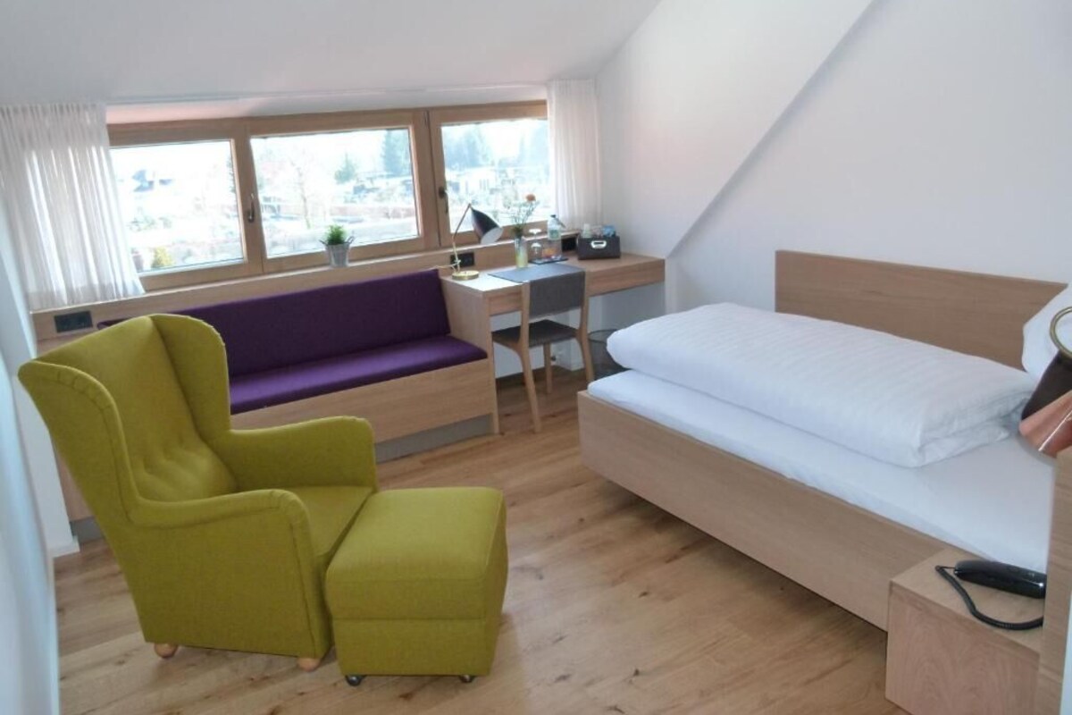 Een moderne kamer met een bed, een bureau, een paarse bank en een groene fauteuil.