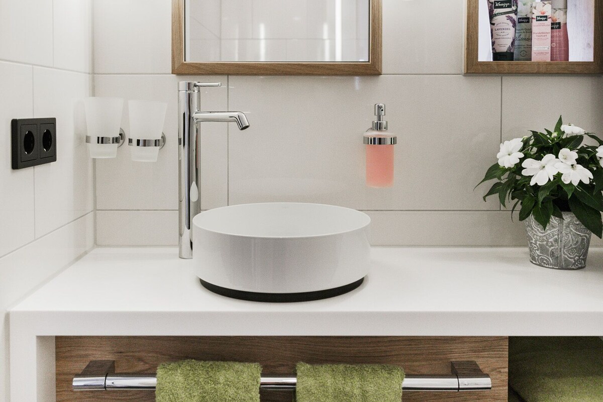 Een moderne badkamer met een witte wasbak, een grote spiegel en twee groene handdoeken.