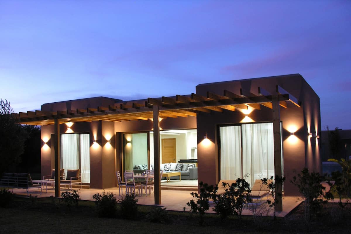 A modern house with a covered patio, large windows, and a well-lit interior.