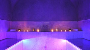 A spa room with a large bathtub, multiple candles, and a stone wall. - Villa Jardins d'Isa (Marrakech)