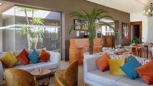 A modern hotel lobby with a large seating area, a reception desk, and a large window overlooking palm trees. - Villa Jardins d'Isa (Marrakech)
