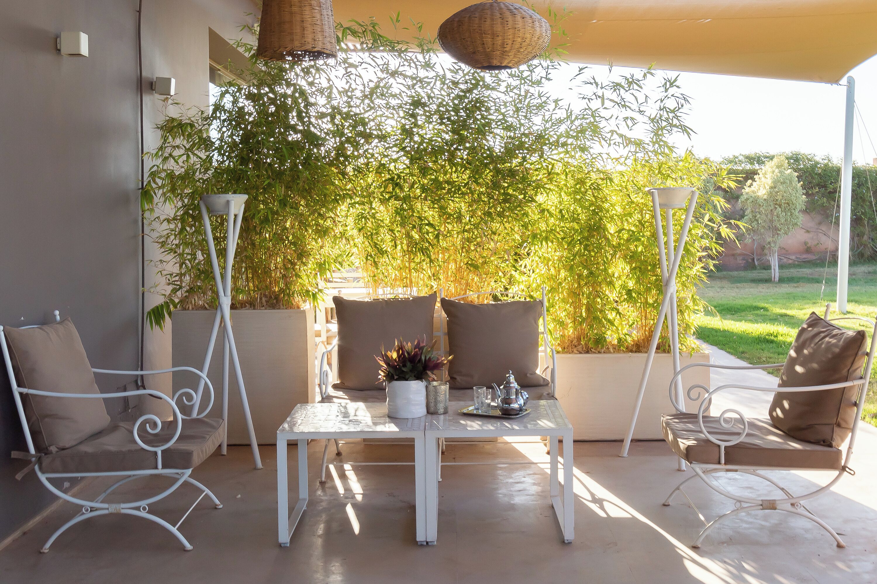 An outdoor patio with white metal furniture, including two chairs and a table, set against a backdrop of bamboo plants.