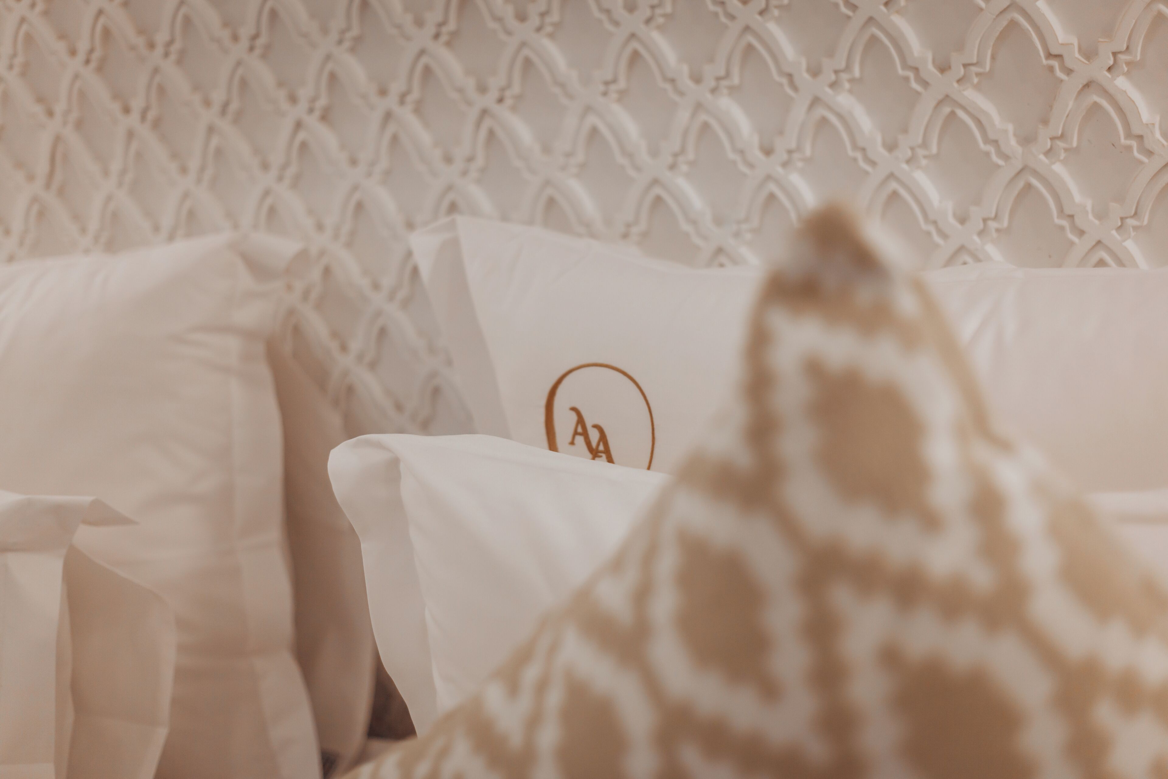 A bed with white bedding and a logo on the headboard.