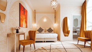 A bedroom with a bed, two chairs, a table, a mirror, and a painting on the wall.