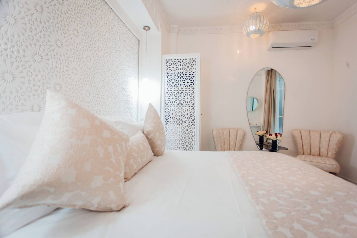 Une chambre à coucher comprenant un lit, deux chaises, un miroir et un paravent décoratif.