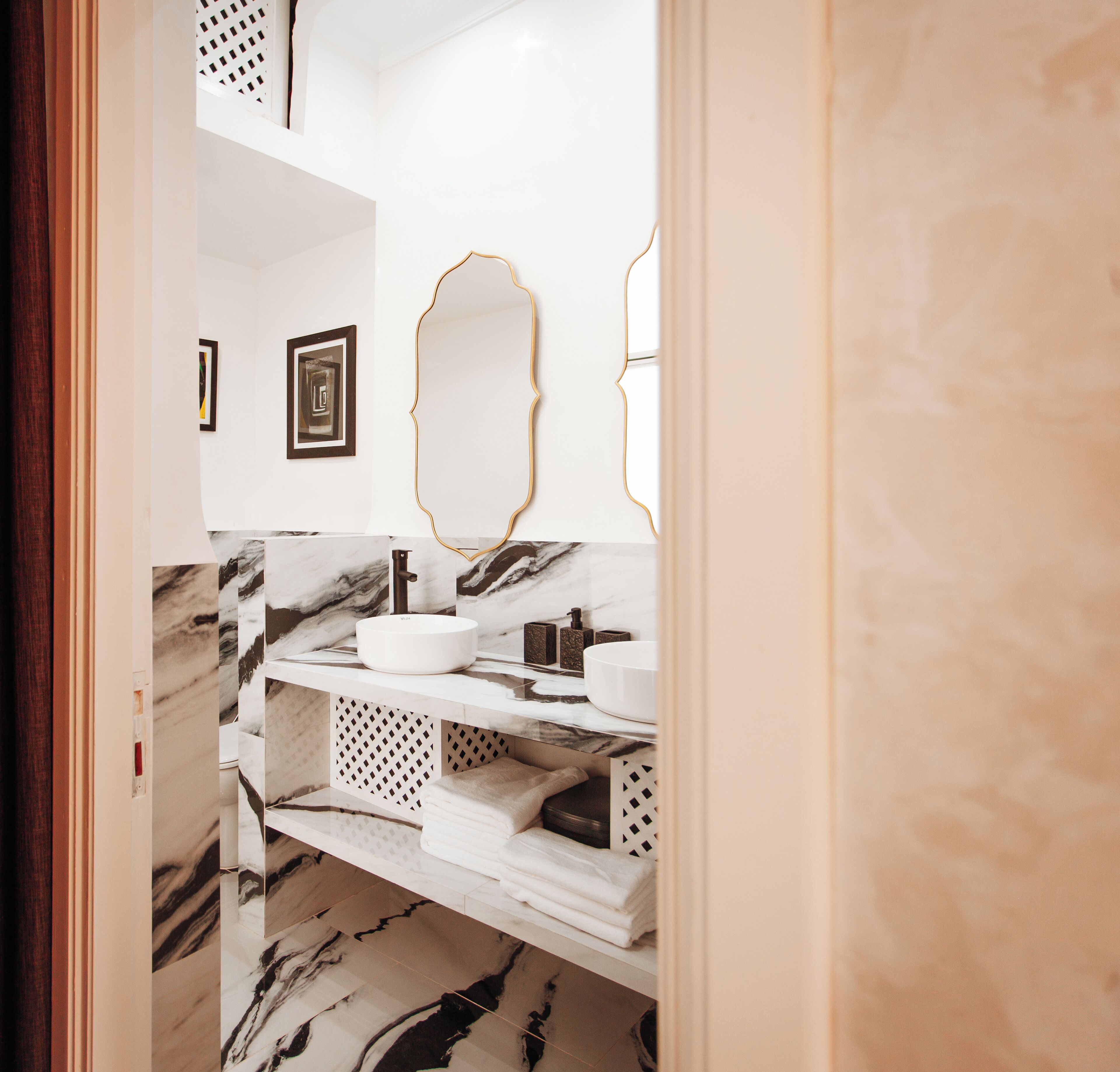 Une salle de bain avec un meuble-lavabo en marbre, un miroir encadré d’or et des serviettes soigneusement pliées, rangées sur des étagères.