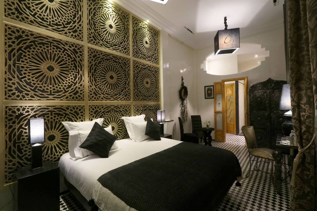 Une chambre d’hôtel avec un grand lit, un panneau décoratif au mur, un bureau avec une lampe et une chaise.