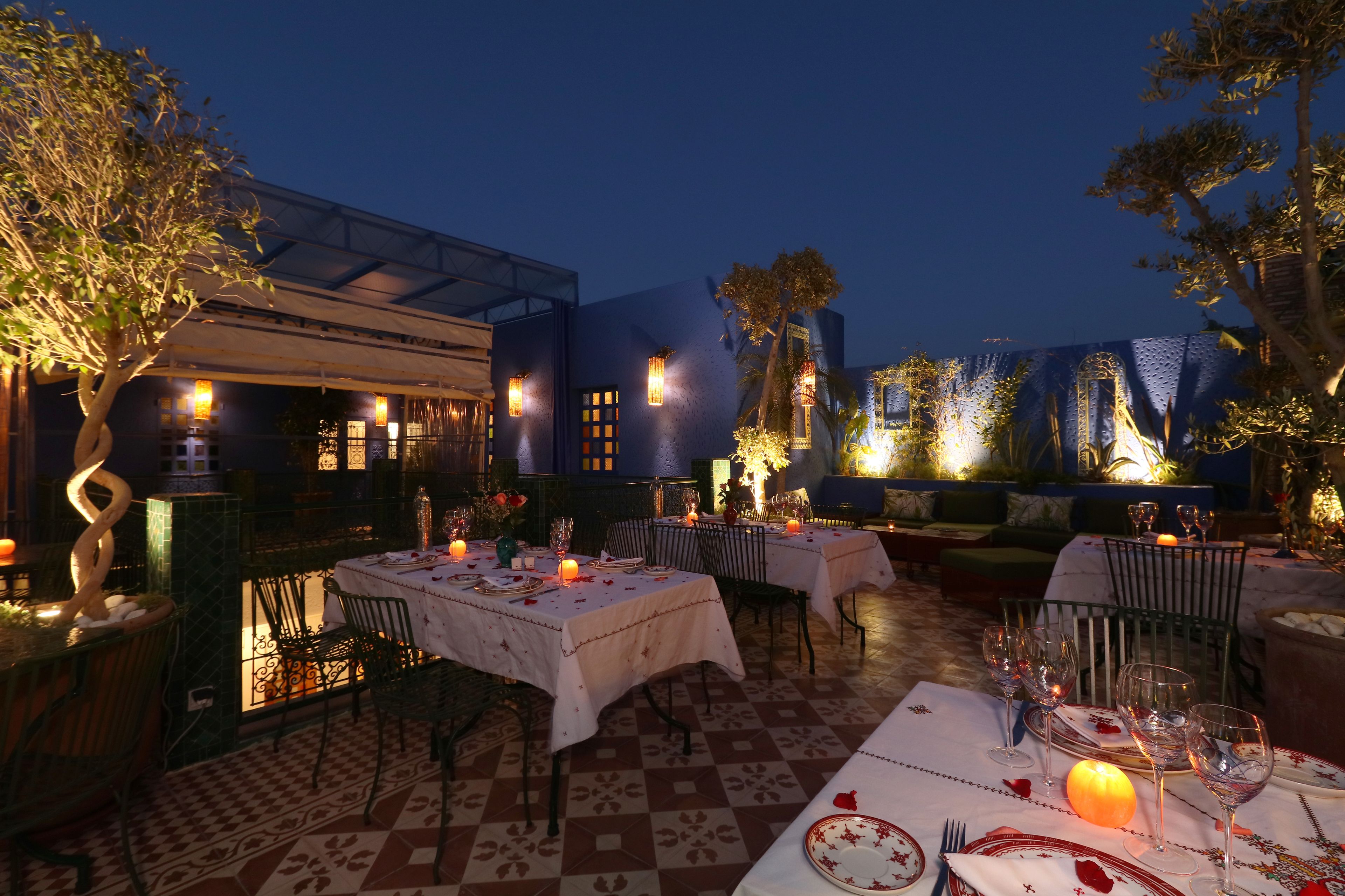 An outdoor dining area with tables set for two, featuring white tablecloths and candle centerpieces.