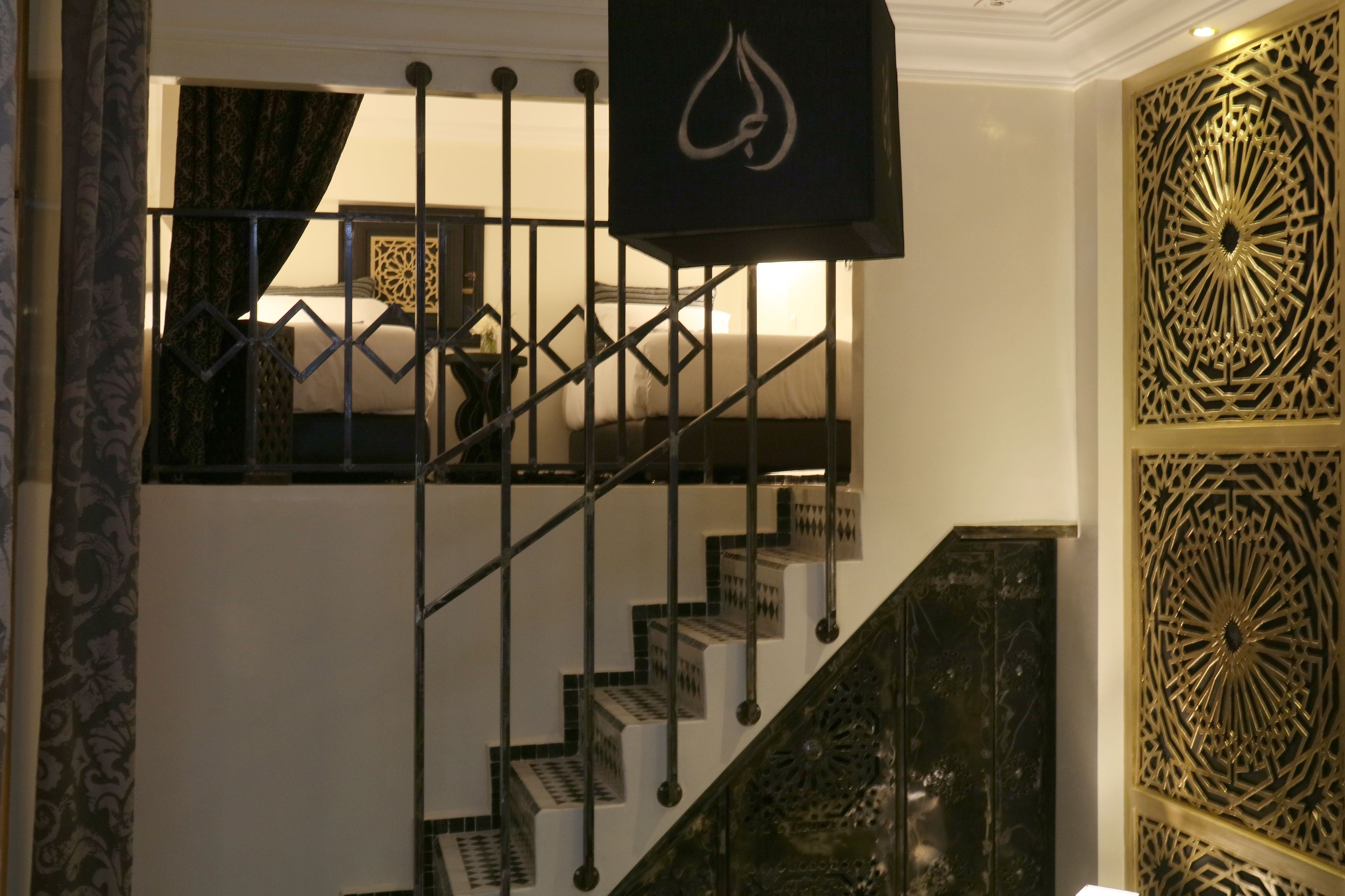 A staircase with a geometric railing design, a patterned wall panel, and a hanging light fixture.