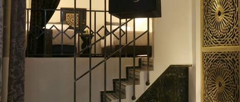 A staircase with a geometric railing design, a patterned wall panel, and a hanging light fixture.