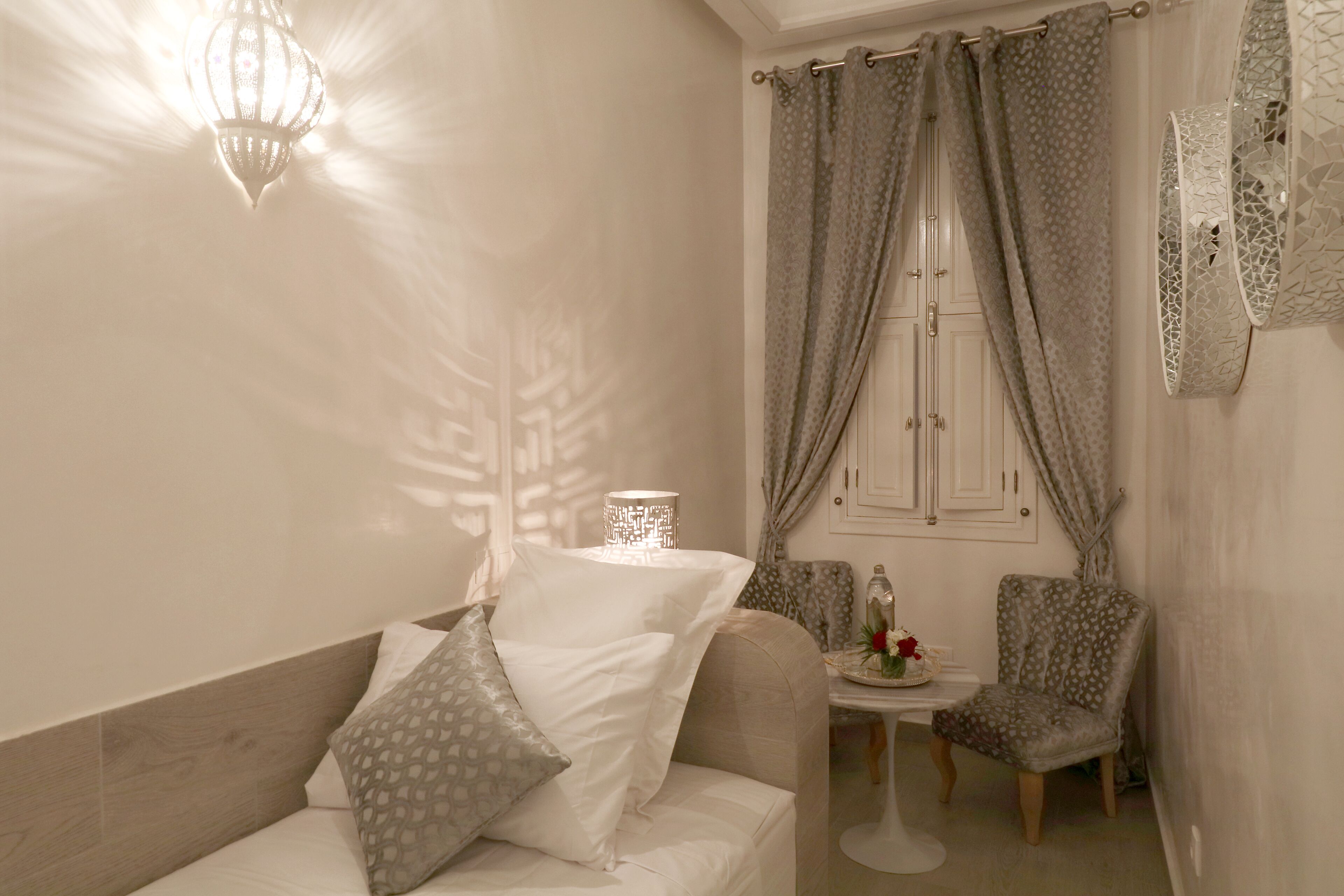 A room with a sofa, two chairs, a table with a vase, and a window with curtains.