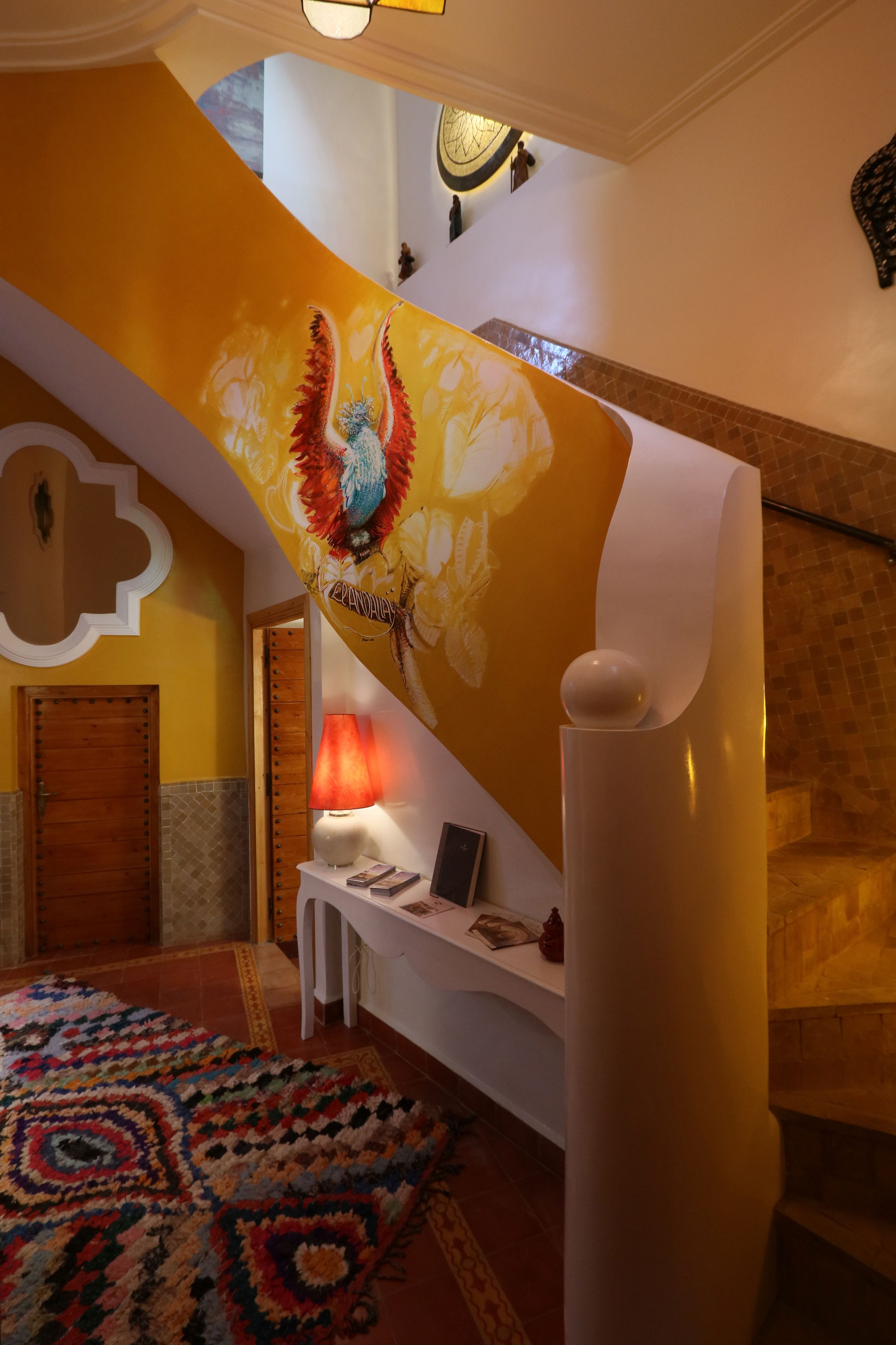 A staircase with a vibrant yellow carpet and a large mural. A white column with a spherical ornament is in the foreground.