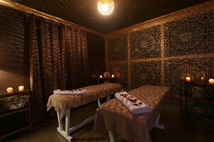 Una stanza spa con due lettini da massaggio, candele e decorazioni elaborate alle pareti.
