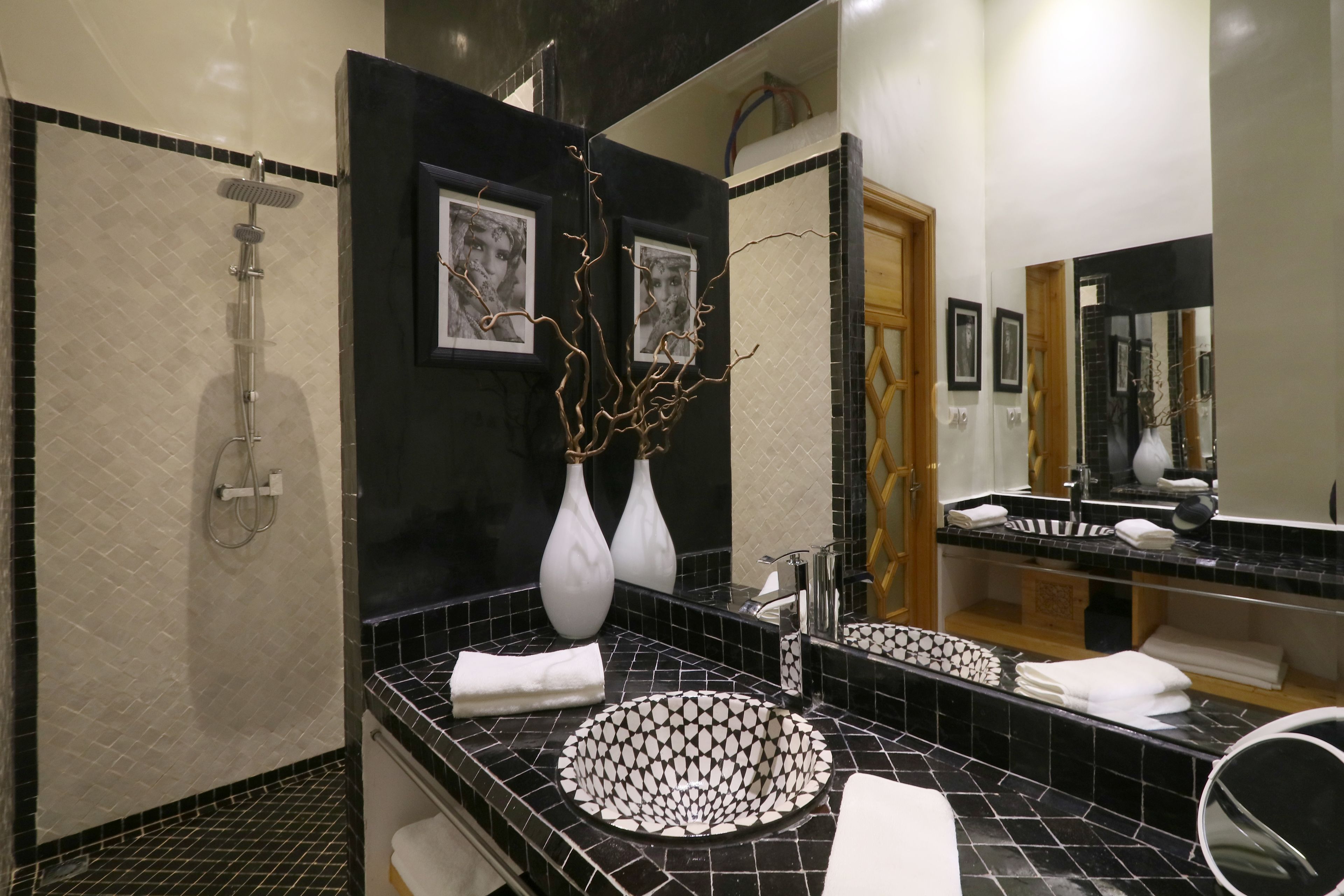 A modern bathroom with a black and white tiled sink, a shower, and a large mirror.