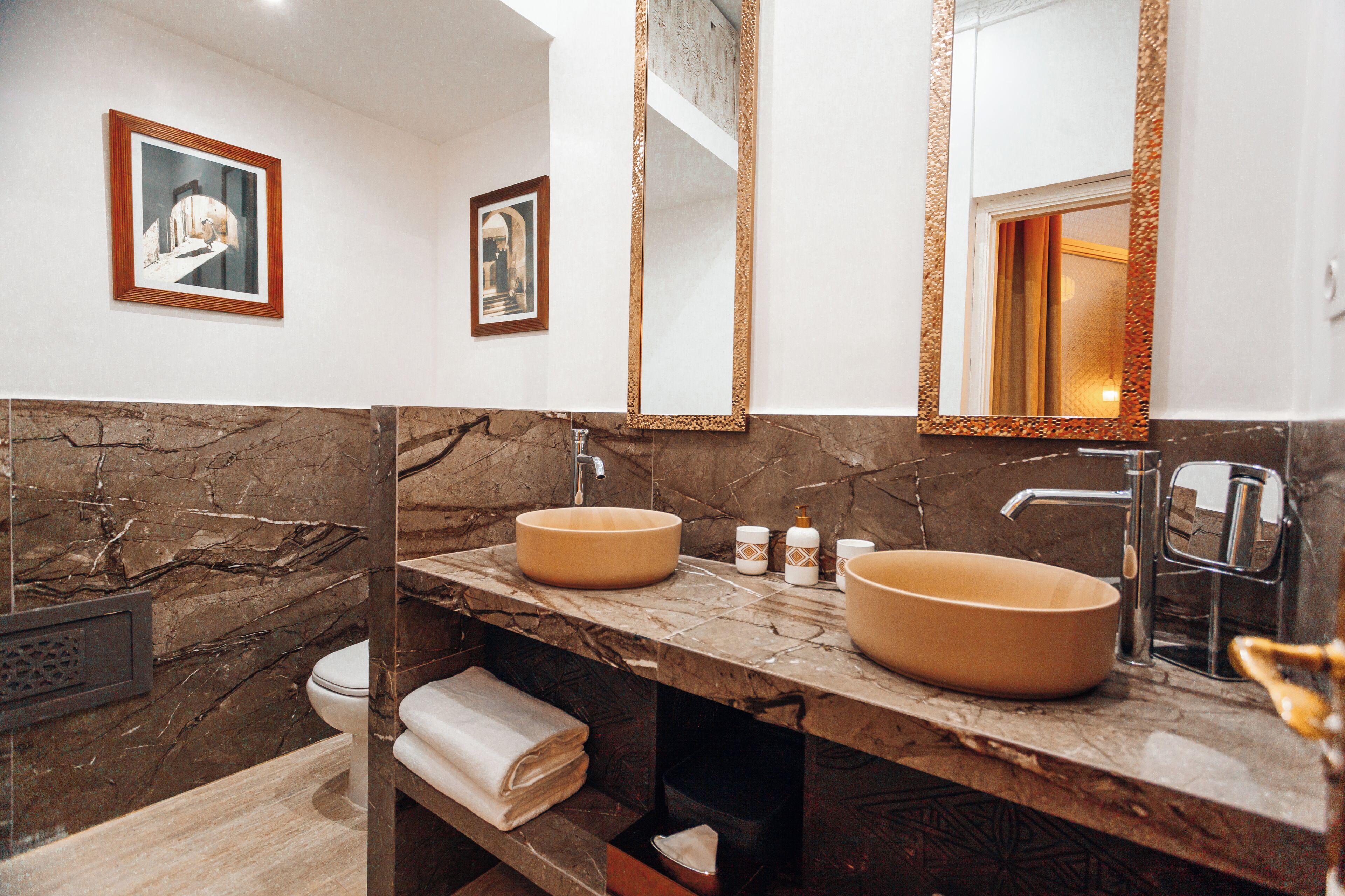 A bathroom with two sinks, marble walls, a large mirror, and a toilet.