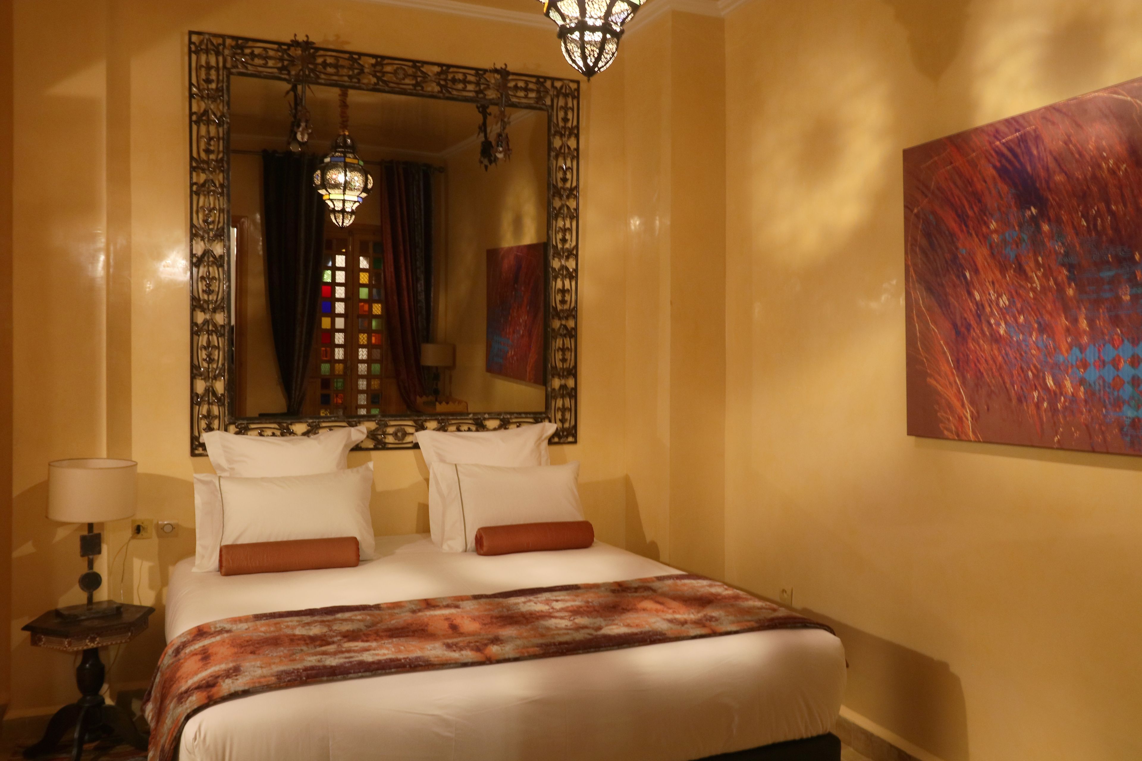 A hotel room with a large bed, a mirror, a painting, and a chandelier.