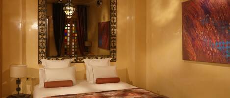 A hotel room with a large bed, a mirror, a painting, and a chandelier.