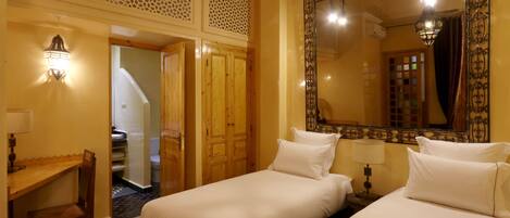 A hotel room with two beds, a desk, and a chair. There is a large mirror on the wall and a staircase leading to another room.